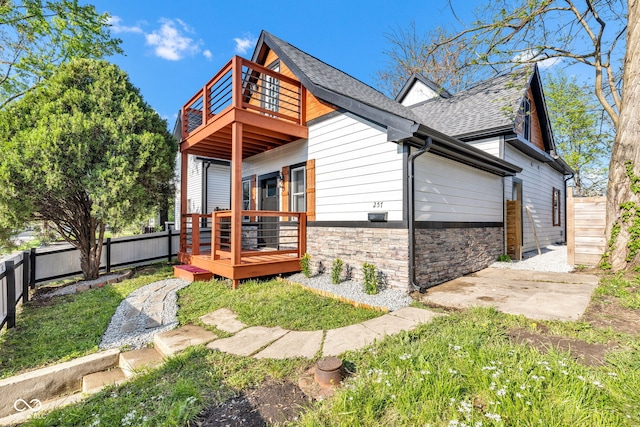 257 N Tacoma Ave, Indianapolis, IN 46201 - rear view of house with stone siding, a wooden deck, a shingled roof, a fenced backyard, and a balcony