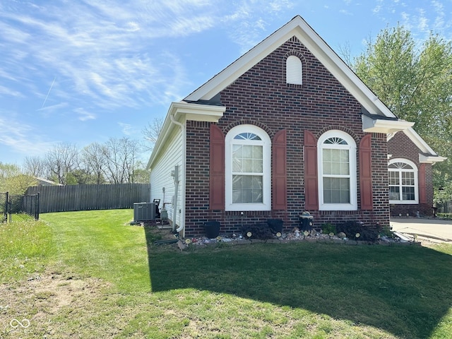 view of side of home featuring brick siding, fence, central AC unit, and a lawn