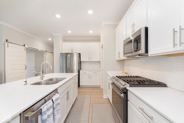 kitchen with crown molding, a barn door, a sink, white cabinets, and stainless steel appliances