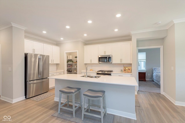 kitchen featuring a kitchen island with sink, appliances with stainless steel finishes, a sink, white cabinets, and light wood finished floors