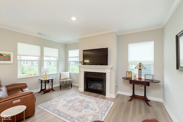 living room with visible vents, crown molding, baseboards, light wood finished floors, and a glass covered fireplace