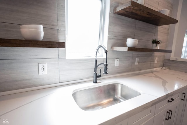 kitchen with light stone counters, white cabinetry, tasteful backsplash, open shelves, and a sink