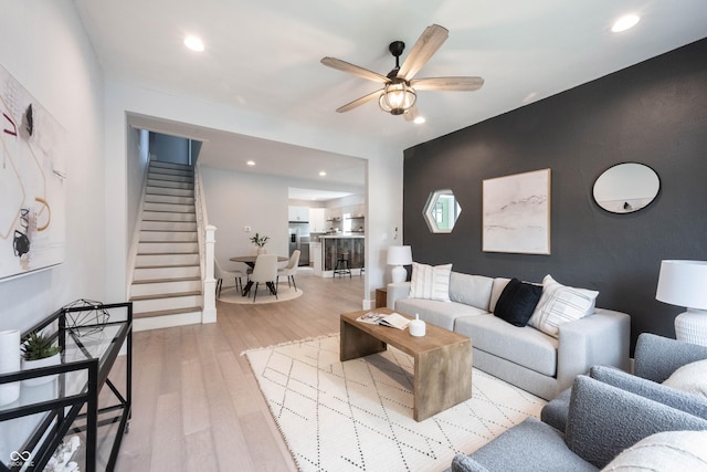 living area with recessed lighting, stairway, ceiling fan, an accent wall, and wood finished floors
