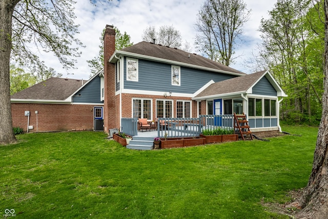 back of property featuring a chimney, a deck, a sunroom, brick siding, and a yard