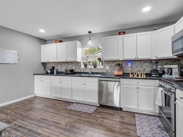 kitchen featuring decorative backsplash, stainless steel appliances, white cabinets, dark countertops, and a sink