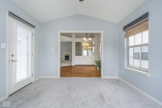carpeted empty room with baseboards, plenty of natural light, a notable chandelier, and vaulted ceiling