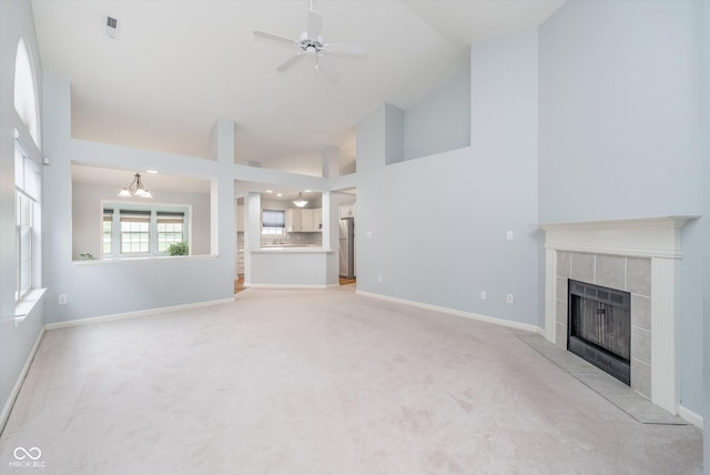unfurnished living room featuring high vaulted ceiling, a fireplace, ceiling fan with notable chandelier, and light colored carpet