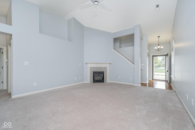 unfurnished living room featuring carpet floors, baseboards, high vaulted ceiling, a tiled fireplace, and ceiling fan with notable chandelier