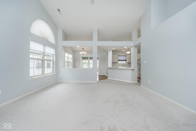 unfurnished living room with visible vents, baseboards, light colored carpet, recessed lighting, and a notable chandelier