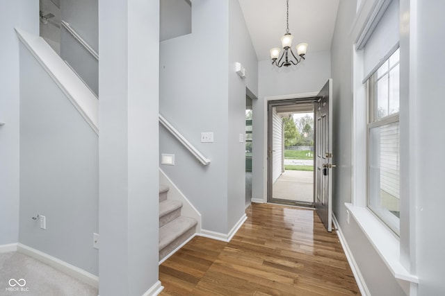 foyer featuring wood finished floors, baseboards, high vaulted ceiling, an inviting chandelier, and stairs