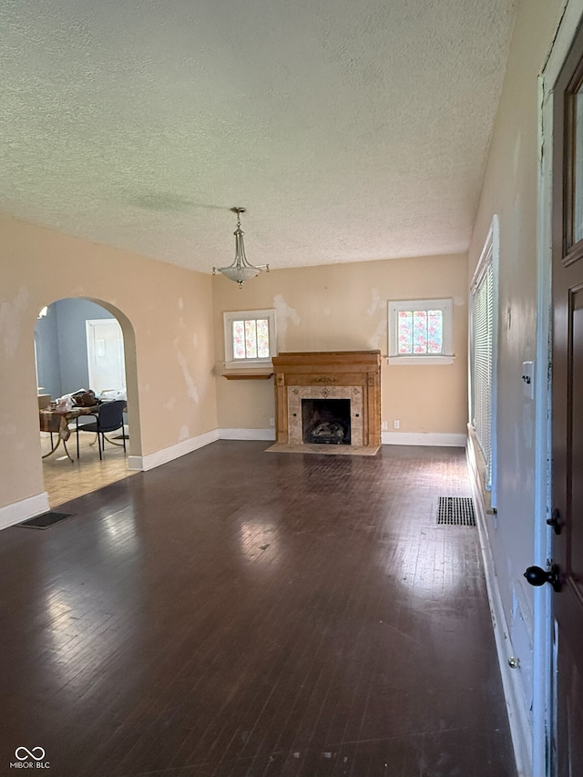 unfurnished living room featuring a textured ceiling, hardwood / wood-style flooring, visible vents, arched walkways, and a tiled fireplace