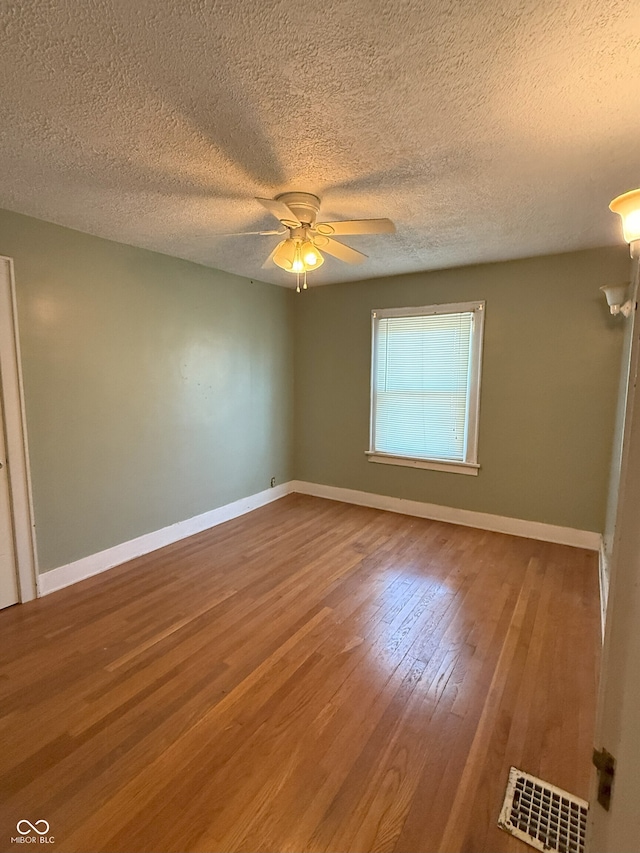 unfurnished room featuring visible vents, wood finished floors, ceiling fan, and a textured ceiling