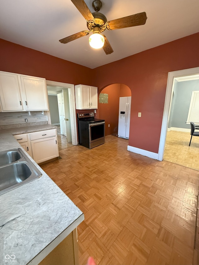 kitchen featuring stainless steel electric range oven, white refrigerator with ice dispenser, a sink, white cabinetry, and a ceiling fan