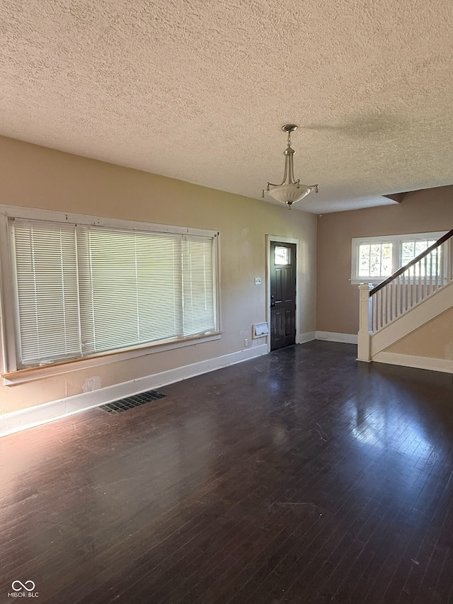 unfurnished living room with stairs, visible vents, baseboards, a textured ceiling, and wood finished floors