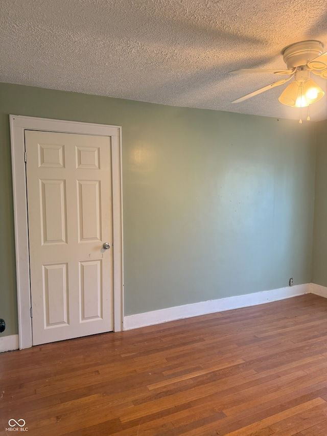 spare room featuring a textured ceiling, wood finished floors, a ceiling fan, and baseboards