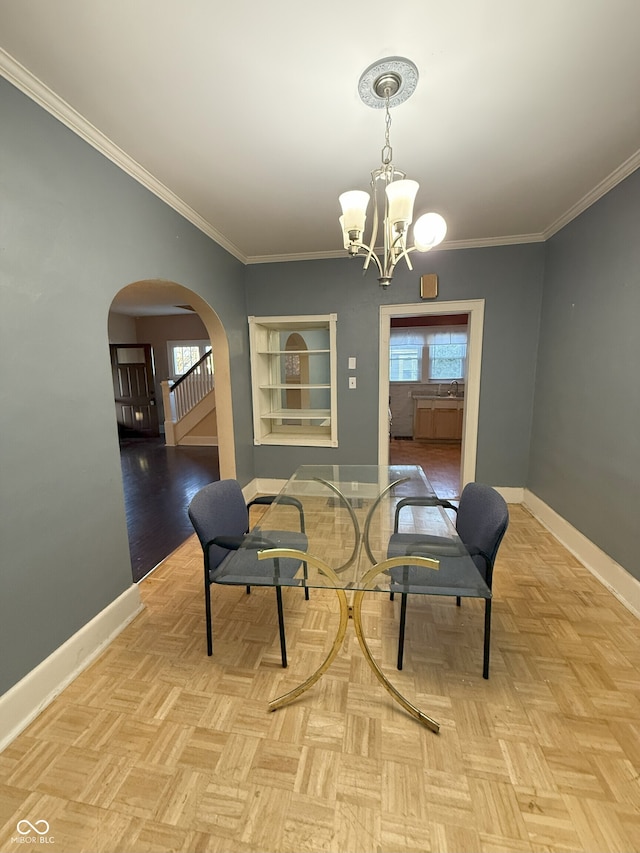 dining space with a chandelier, baseboards, crown molding, and arched walkways