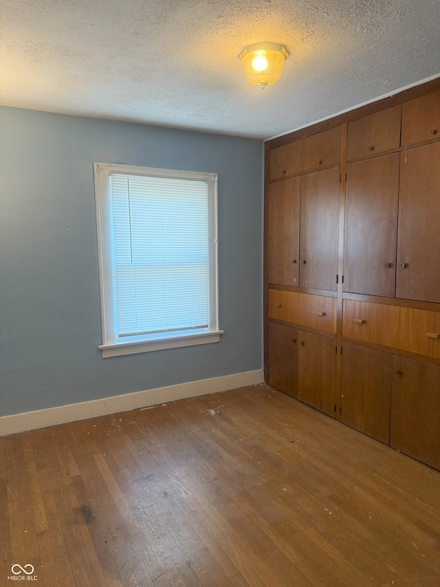 unfurnished bedroom featuring a closet, hardwood / wood-style floors, a textured ceiling, and baseboards