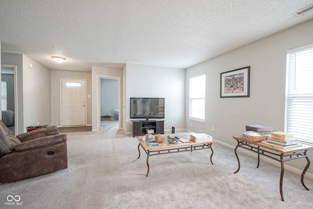 living area with carpet flooring, a textured ceiling, visible vents, and baseboards