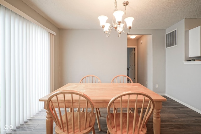 dining space with a textured ceiling, visible vents, wood finished floors, baseboards, and a notable chandelier