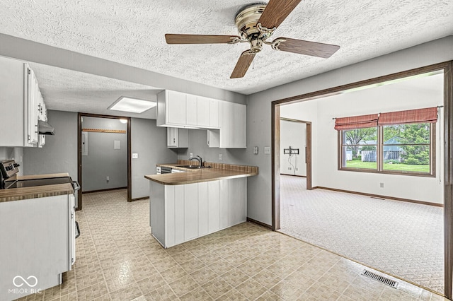 kitchen with a sink, a peninsula, white cabinets, baseboards, and light flooring
