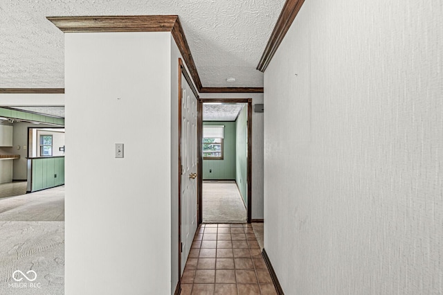 hallway with a textured ceiling, ornamental molding, baseboards, and tile patterned flooring