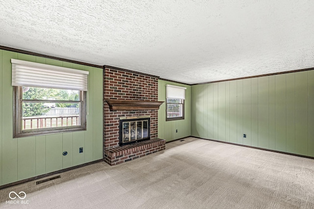 unfurnished living room featuring a textured ceiling, carpet flooring, a fireplace, crown molding, and wooden walls