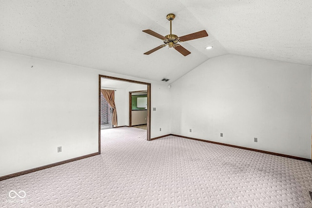 spare room featuring light carpet, a ceiling fan, vaulted ceiling, baseboards, and a textured ceiling