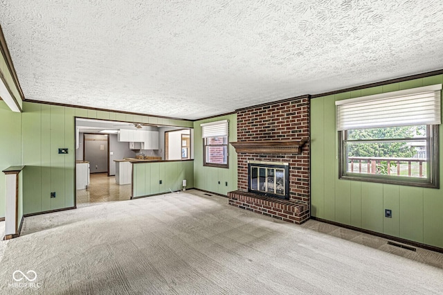 unfurnished living room featuring plenty of natural light, light colored carpet, a fireplace, a textured ceiling, and ornamental molding
