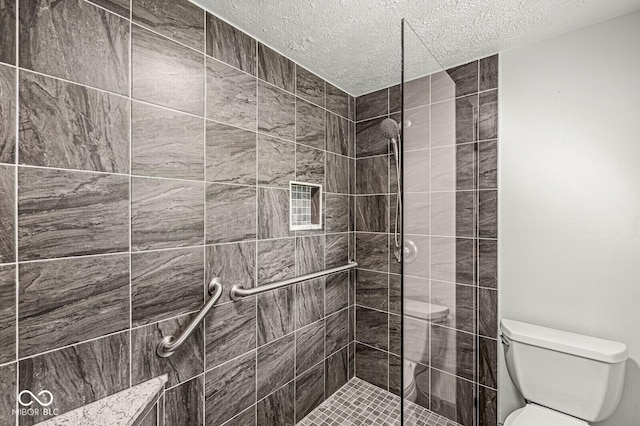bathroom with a textured ceiling, toilet, and tiled shower