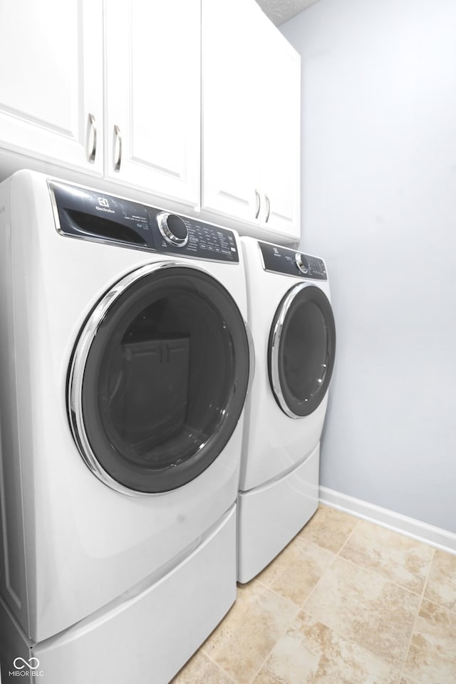 washroom with baseboards, cabinet space, and washing machine and clothes dryer