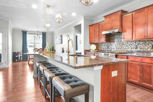 kitchen with a sink, a notable chandelier, ornamental molding, a breakfast bar, and under cabinet range hood