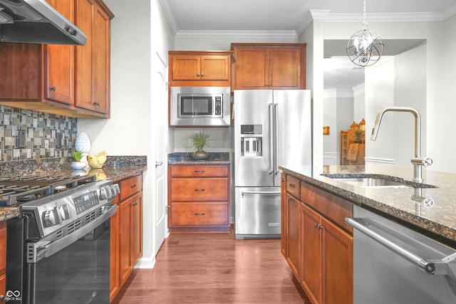 kitchen with dark wood-type flooring, under cabinet range hood, a sink, dark stone countertops, and stainless steel appliances