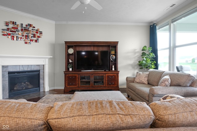 living room with visible vents, ornamental molding, baseboards, a tile fireplace, and a ceiling fan