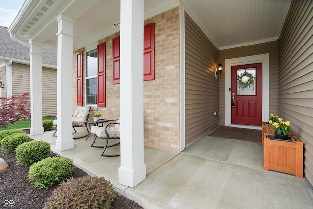 view of exterior entry with a porch and brick siding