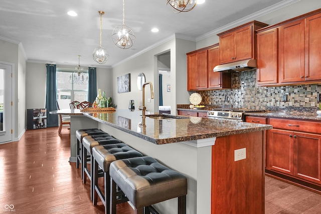 kitchen with crown molding, a notable chandelier, a sink, a kitchen bar, and under cabinet range hood