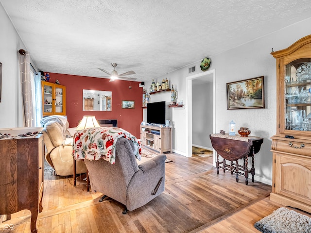 living area featuring light wood-style floors, visible vents, a ceiling fan, and a textured ceiling