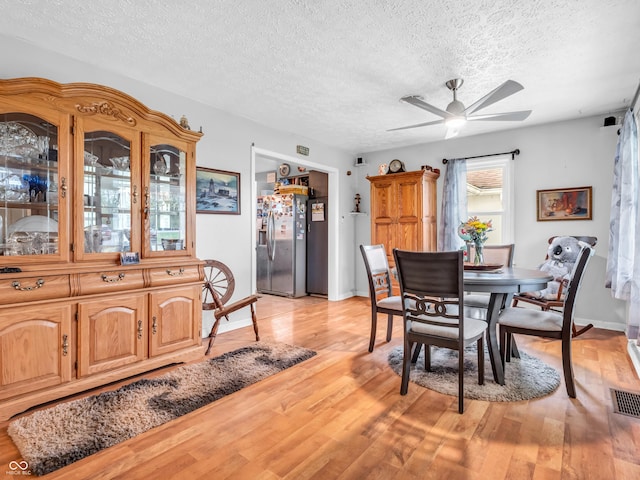 dining space with a ceiling fan, light wood-style flooring, a textured ceiling, and baseboards