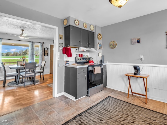 kitchen featuring gray cabinets, stainless steel range with electric cooktop, wainscoting, light countertops, and ceiling fan