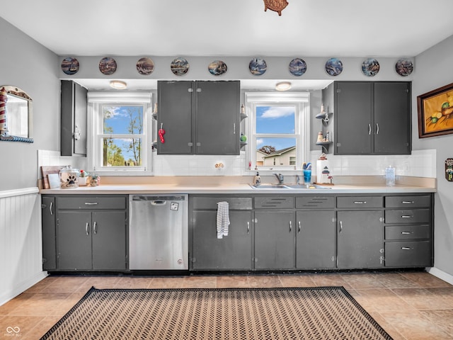 kitchen with a sink, gray cabinets, tasteful backsplash, light countertops, and stainless steel dishwasher