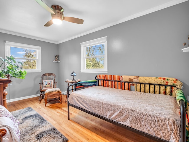 bedroom with ornamental molding, multiple windows, wood finished floors, and baseboards