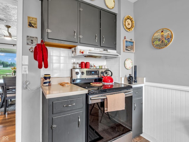 kitchen with light countertops, gray cabinets, under cabinet range hood, stainless steel electric range, and backsplash