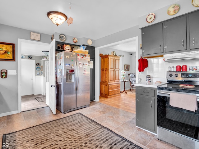 kitchen with gray cabinets, decorative backsplash, stainless steel appliances, under cabinet range hood, and baseboards