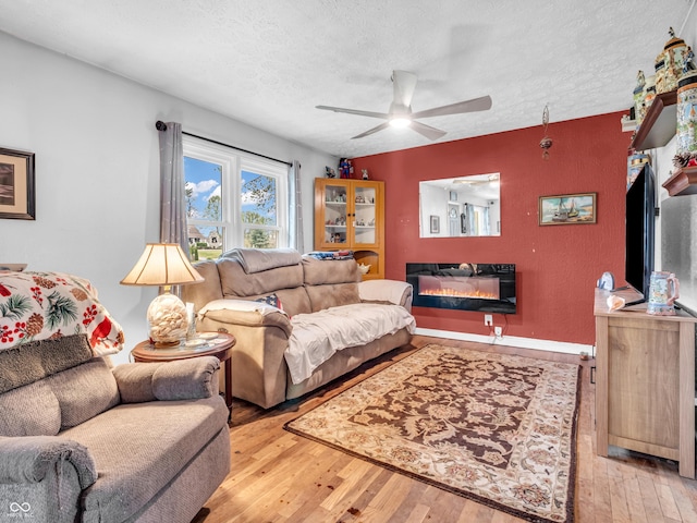 living room with a ceiling fan, a textured ceiling, wood-type flooring, and a glass covered fireplace