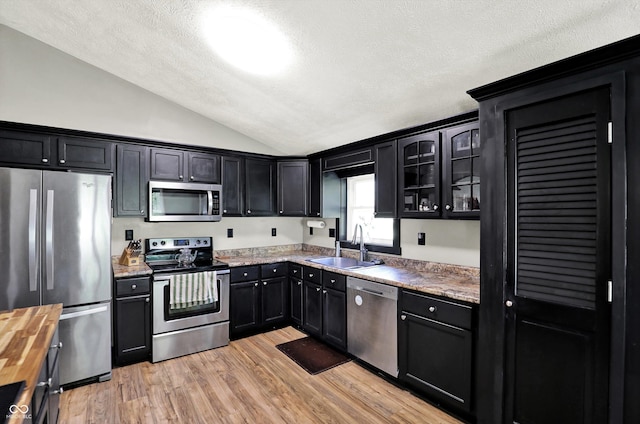 kitchen featuring appliances with stainless steel finishes, a sink, light wood finished floors, a textured ceiling, and lofted ceiling