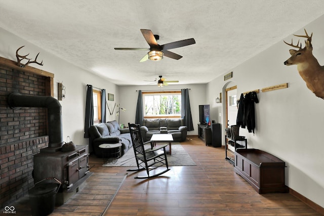 living room featuring ceiling fan, a textured ceiling, visible vents, a wood stove, and dark wood finished floors