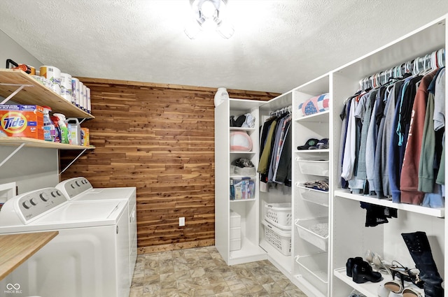 laundry area featuring laundry area, wood walls, a textured ceiling, and washing machine and clothes dryer
