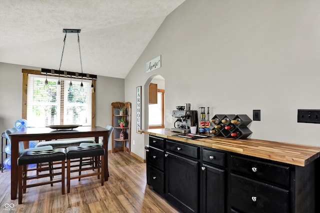 dining space featuring wood finished floors, lofted ceiling, baseboards, a textured ceiling, and arched walkways