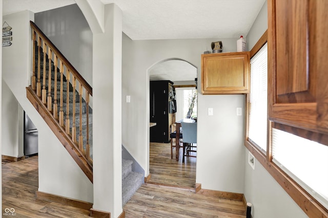 staircase featuring arched walkways, baseboards, and wood finished floors