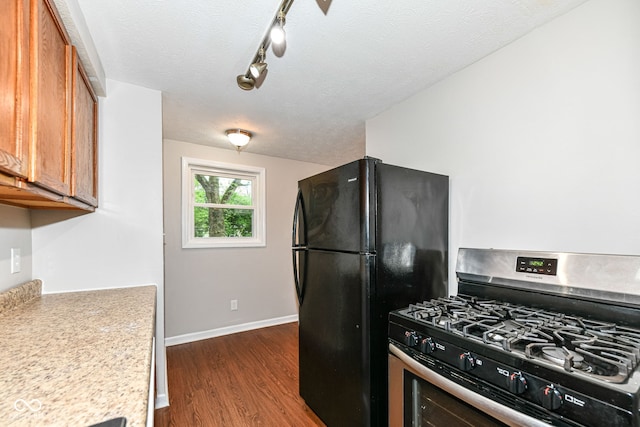 kitchen with stainless steel range with gas stovetop, brown cabinetry, dark wood-type flooring, light countertops, and freestanding refrigerator