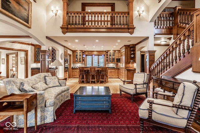 living area featuring decorative columns, arched walkways, stairway, bar area, and a high ceiling